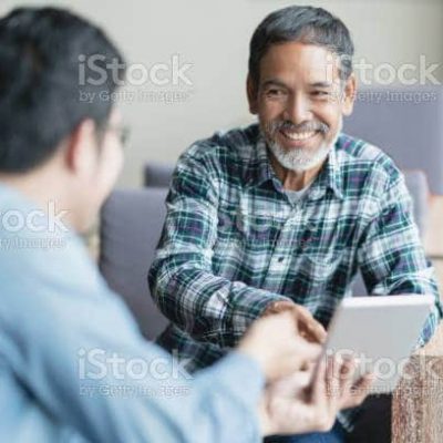 Happy old short beard asian man sitting, smiling and listen to partner that showing presentation on smart digital tablet. Mature man with social media technology teaching or urban lifestyle concept.