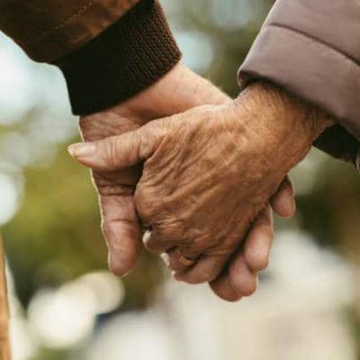 Close up of elderly couple holding hands and walking outdoors. Rear view of man and woman holding hands of each other while walking outdoors.