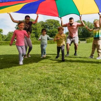 Children playing with a parachute at school during pe in the North East of England, holding it up and running under it.