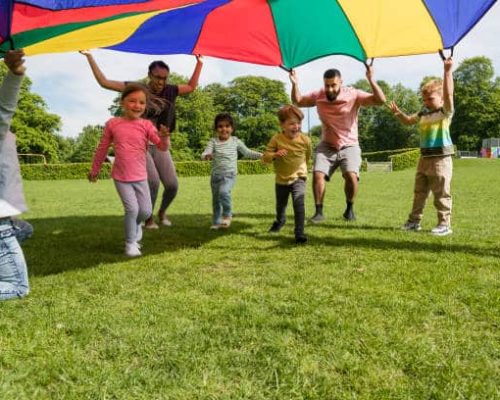 Children playing with a parachute at school during pe in the North East of England, holding it up and running under it.