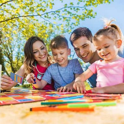 Smiling parents playing board game with their son and daughter and enjoying in spring day outdoors.